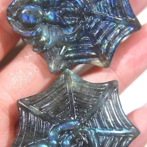May include: Two iridescent blue labradorite gemstone carvings of spiders in spiderwebs. The carvings are detailed and show the spiders in a realistic pose.