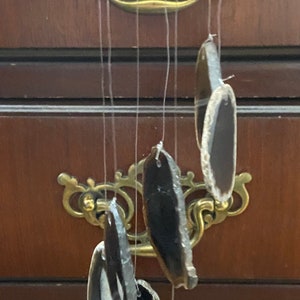 May include: A wooden wind chime with agate slices hanging from it. The agate slices are brown, black, and white. The wind chime is hanging from a wooden ceiling.