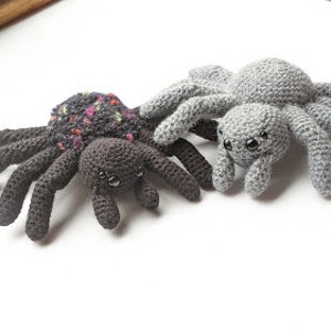 May include: Two crocheted spider toys, one black with multi-colored accents and one gray. Both have black eyes and eight legs.