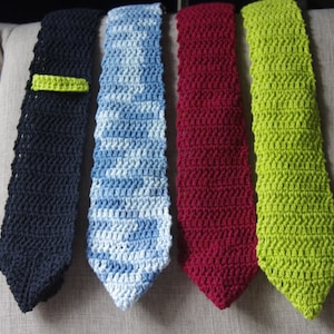 May include: Four crocheted ties in different colours: black, blue, red, and green. The ties are arranged in a row on a light brown surface.