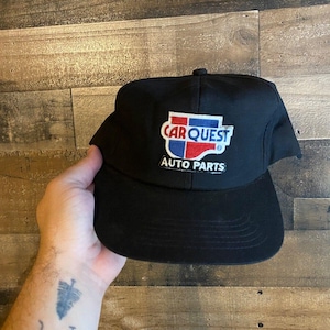 May include: Black baseball cap with a red, white, and blue Carquest Auto Parts logo.