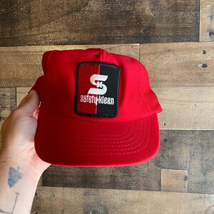 Peut inclure: Casquette de baseball rouge avec un patch noir et blanc qui dit "Safety-Kleen" avec un "S" blanc au centre.