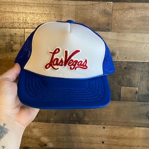 May include: A blue and white trucker hat with a red and white embroidered "Las Vegas" logo.