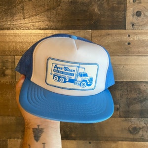 Peut inclure: Un chapeau de camionneur bleu et blanc avec un patch représentant un camion bleu avec le texte "Aqua-Clean Mobile Wash Services Ltd. Edmonton, Grande Prairie"