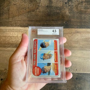 Könnte beinhalten: Eine Baseballkarte in einer transparenten Kunststoffhülle. Die Karte zeigt drei Baseballspieler: Ken Harrelson, Willie Horton und Frank Howard. Die Karte trägt die Aufschrift "1968 Home Run Leaders" und "American League."