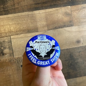 May include: A blue button with a white outline and the text "Pat Croce's I Feel Great Show" with a cartoon image of a man in a white shirt and black jacket with the text "Diet Pepsi Presents" and "Spectrum" on the button.