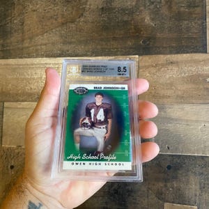 Könnte beinhalten: Eine Brad Johnson Footballkarte aus der 2000 Donruss Pref Graded Serie, bewertet mit 8,5. Die Karte zeigt ein Foto von Brad Johnson in seiner Highschool-Football-Uniform mit dem Text "High School Profile" und "Owen High School".