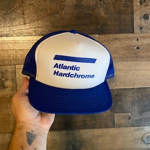 May include: A white and blue trucker hat with a blue stripe and the text "Atlantic Hardchrome" in blue letters.
