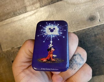 May include: A rectangular Disney Channel pin with a purple background. The pin features an illustration of Goofy in a red robe, with the Disney Channel logo at the top. The text "The Disney Channel" is above the logo. The pin is held in a hand.