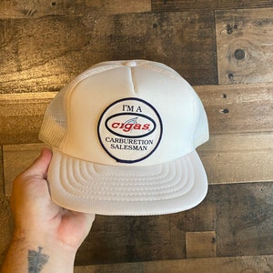 Può includere: Cappellino da camionista bianco con una toppa blu e rossa che dice "I'm a Cig-as Carburetor Salesman".