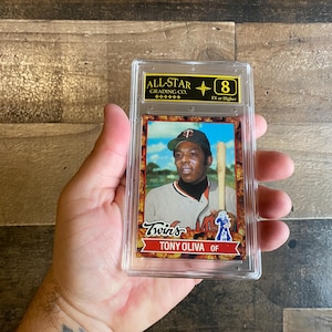 Könnte beinhalten: Eine Baseball-Sammelkarte mit Tony Oliva von den Minnesota Twins, bewertet mit einer 8 von All-Star Grading Co. Die Karte ist in einem transparenten Kunststoffhalter eingeschlossen, mit einem Porträt von Oliva in seinem Twins-Trikot.