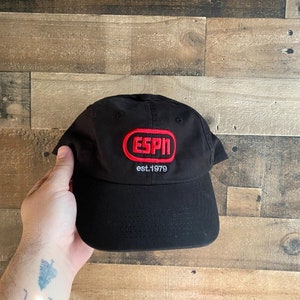 May include: Black baseball cap with a red oval patch that says "ESPN est. 1979" in white lettering.