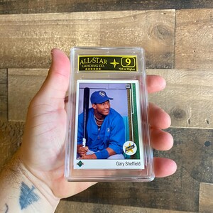 Puede incluir: Una tarjeta de béisbol de Gary Sheffield, calificada por All-Star Grading Co. La tarjeta presenta una imagen en color de Sheffield con uniforme azul, sosteniendo un bate. La tarjeta está dentro de un soporte de plástico transparente con una calificación de 9.