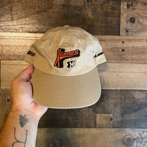 May include: A tan baseball cap with a black and orange embroidered logo that says "Games X" and "LA Angels" on the side.