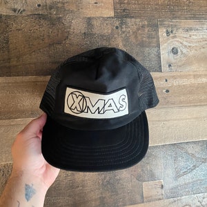Peut inclure: Casquette de camionneur noire avec un logo "XMAS" blanc sur le devant.