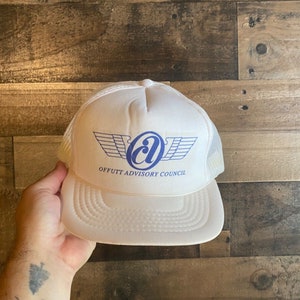May include: White trucker hat with a curved brim and mesh back. The hat features a blue and white logo with the text "OFFUTT ADVISORY COUNCIL". The hat is made of a soft, breathable material.