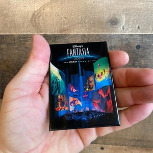 May include: A black button featuring a collage of images from the Disney film Fantasia 2000. The text "Disney's Fantasia 2000 The IMAX Experience" is printed on the button.