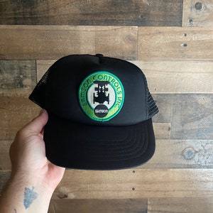 Peut inclure: Casquette de camionneur noire avec un patch brodé vert et blanc qui dit "Samson Controls Inc."