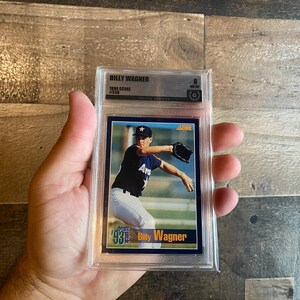 May include: A baseball card of Billy Wagner, graded as an 8 by a grading company. The card features a photo of Wagner in his Astros uniform. The card is encased in a clear plastic holder.