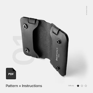 Puede incluir: Cartera de cuero negro con un diseño minimalista. La cartera tiene una solapa plegable con cierre a presión y el texto "DARKSAILS PARIS" grabado en la parte delantera.