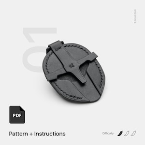 May include: A black leather accessory with a cross-shaped design and a stitched border. The accessory has a loop and a cross-shaped design. The image includes the text "Pattern + Instructions" and a PDF icon.
