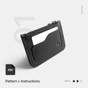 Puede incluir: Cartera de cuero negro con cremallera, una ranura para tarjetas y un bolsillo pequeño. La cartera tiene un logotipo triangular y un icono PDF con el texto "Pattern + Instructions".