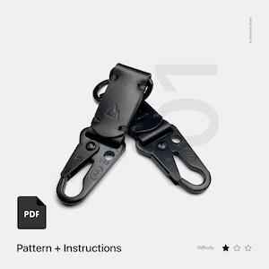 May include: Two black leather keychains with metal clips. The keychains have a stitched design and a small triangle logo. The text "PDF" and "Pattern + Instructions" are visible in the image. The difficulty level is indicated by one star.