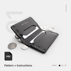 May include: Black leather wallet with a minimalist design. The wallet is open and shows two card slots. The text "CARDS" is printed on the front of the wallet. The wallet is surrounded by coins.