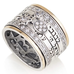 May include: A silver and gold spinning ring with a Hebrew inscription, a star of David, and a pomegranate design. The ring is set with clear cubic zirconia stones.
