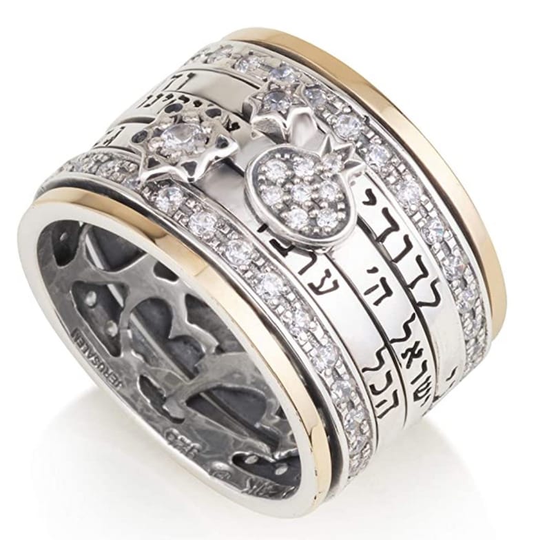 May include: A silver and gold spinning ring with a Hebrew inscription, a star of David, and a pomegranate design. The ring is set with clear cubic zirconia stones.
