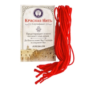 May include: A red string with a certificate card. The card has a picture of the Western Wall in Jerusalem and text in Russian that reads "Red String Certificate" and "Protects from the evil eye and drives away evil spirits. May God bless you and keep you. Jerusalem."