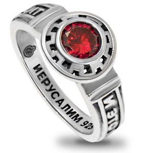 May include: A silver ring with a red gemstone set in a circular bezel. The ring is inscribed with the words "Jerusalem 925" and "Magdala".