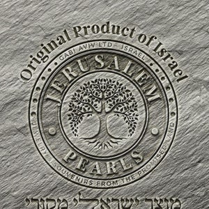 May include: A circular stone emblem with the words "Original Product of Israel" and "Jerusalem Pearls Jewelry & Souvenirs from the Promised Land" surrounding a tree of life design. The text "מוצר ישראלי מקורי" is below the emblem.
