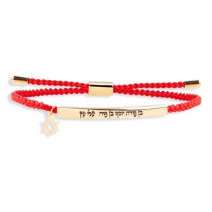 Könnte beinhalten: Rotes Armband mit einem goldenen Anhänger mit den hebräischen Worten "Mi Shebeirach" und einem Davidstern.