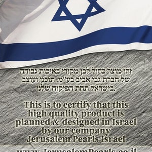 May include: A close-up of a gray stone surface with a blue and white Israeli flag draped over it. The flag has a Star of David in the center. The text "This is to certify that this high quality product is planned & designed in Israel by our company Jerusalem Pearls Israel www.JerusalemPearls.co.il" is printed below the flag.