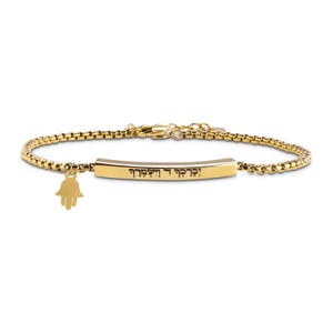 May include: Gold-toned bracelet with a rectangular bar and a small Hamsa hand charm. The bar features engraved text. The bracelet has a box chain design and a clasp closure. A stylish piece of jewelry.