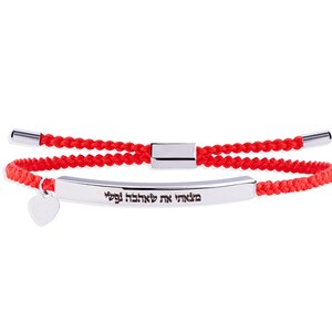 May include: Red braided bracelet with a silver bar and heart charm. The silver bar has Hebrew text. The bracelet has a sliding knot closure with silver metal ends. A simple and elegant piece of jewellery.