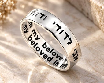 May include: A polished silver band ring featuring black engraved Hebrew text on the outer surface and the English phrase "I am my beloved and my beloved is mine" clearly inscribed in black lettering along the inner circumference of the band.