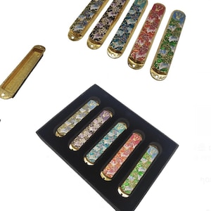 May include: Set of six colorful mezuzah cases with floral designs and gold accents. The cases are arranged in a black box with a velvet lining. Each case features a Star of David and a Hebrew inscription.