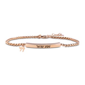 Könnte beinhalten: Roségoldenes Armband mit einem rechteckigen Steg, der mit hebräischen Texten graviert ist, und einem kleinen Anhänger. Das Armband hat ein filigranes Kettendesign und einen Karabinerverschluss. Der Anhänger ist ein kleines, stilisiertes Symbol.