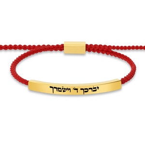 Può includere: Braccialetto in corda rossa con un ciondolo a barra dorata che dice "לבקר לי ולשמור" in ebraico.
