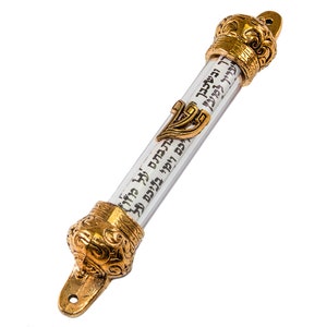 May include: A gold-colored mezuzah with a clear glass tube containing a scroll of Hebrew text. The mezuzah has a decorative crown at the top and a menorah design at the bottom.