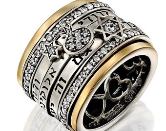 May include: A silver and gold ring with a spinning band featuring Hebrew text, a Star of David, and a small, clear crystal heart. The ring is adorned with clear crystals.