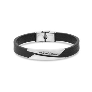 Puede incluir: Un brazalete de cuero negro con una banda de metal plateado grabada con texto hebreo. El brazalete tiene un cierre de metal plateado.
