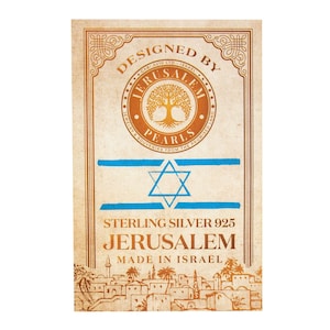 May include: A vintage-style label with a gold and blue design. The label reads "Designed by Jerusalem Pearls Jewelry & Souvenirs from the Promised Land." It also features a star of David and the text "Sterling Silver 925 Jerusalem Made in Israel".