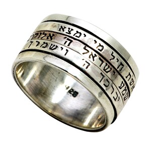 May include: A silver ring with Hebrew text inscribed on the band. The ring has a spinning band with four lines of text.