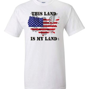 May include: White t-shirt with a graphic of the United States map in the shape of an eagle with the American flag design. The text "This Land is My Land" is printed below the graphic.