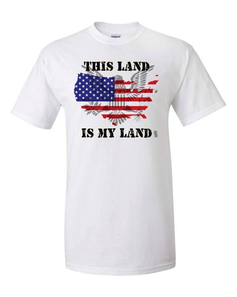 May include: White t-shirt with a graphic of the United States map in the shape of an eagle with the American flag design. The text "This Land is My Land" is printed below the graphic.