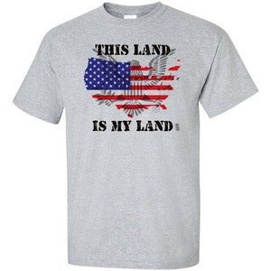 May include: A grey t-shirt with the text "This Land Is My Land" printed in black. The text is surrounded by a graphic of the United States map with the American flag superimposed on it.