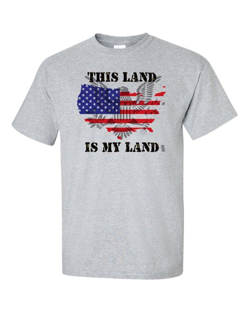 May include: A grey t-shirt with the text "This Land Is My Land" printed in black. The text is surrounded by a graphic of the United States map with the American flag superimposed on it.